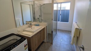 Ein modernes Badezimmer mit großem Spiegel, zwei Waschbecken, einer Duschkabine und einer integrierten Waschmaschine.