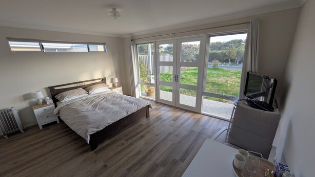 Ein Schlafzimmer mit Bett, Fernseher, Schreibtisch mit Tablett und Blick auf Grün durch große Fenster.