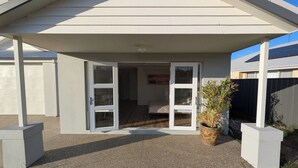 Ein modernes Haus mit überdachter Veranda, einem Blumentopf und einem sichtbaren Schlafzimmer mit Bett und Fenster.