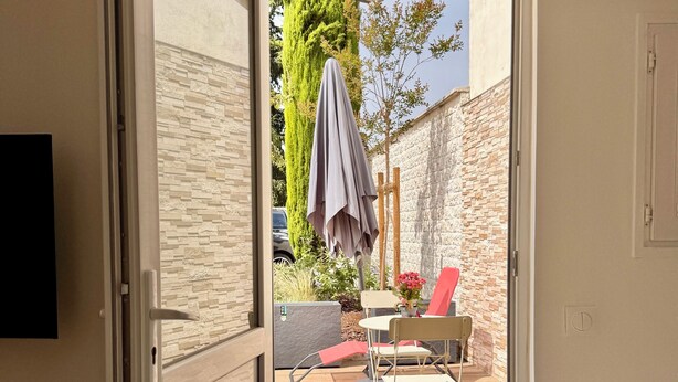 An open sliding door leading to a patio with a table, chairs, and a covered area. - Lovely self-contained studio in Roissy-en-France / Aeroport CDG with airport terrace (Roissy-en-France)