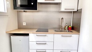 A compact kitchen with white cabinets, a black microwave, a stainless steel sink, and a small refrigerator. - Lovely self-contained studio in Roissy-en-France / Aeroport CDG with airport terrace (Roissy-en-France)