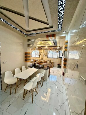 A modern dining area with a marble floor, white chairs, and a long table.
