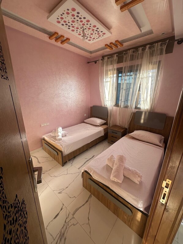 A bedroom with two single beds, a wooden wardrobe, a ceiling with a decorative pattern, and a window with sheer curtains.