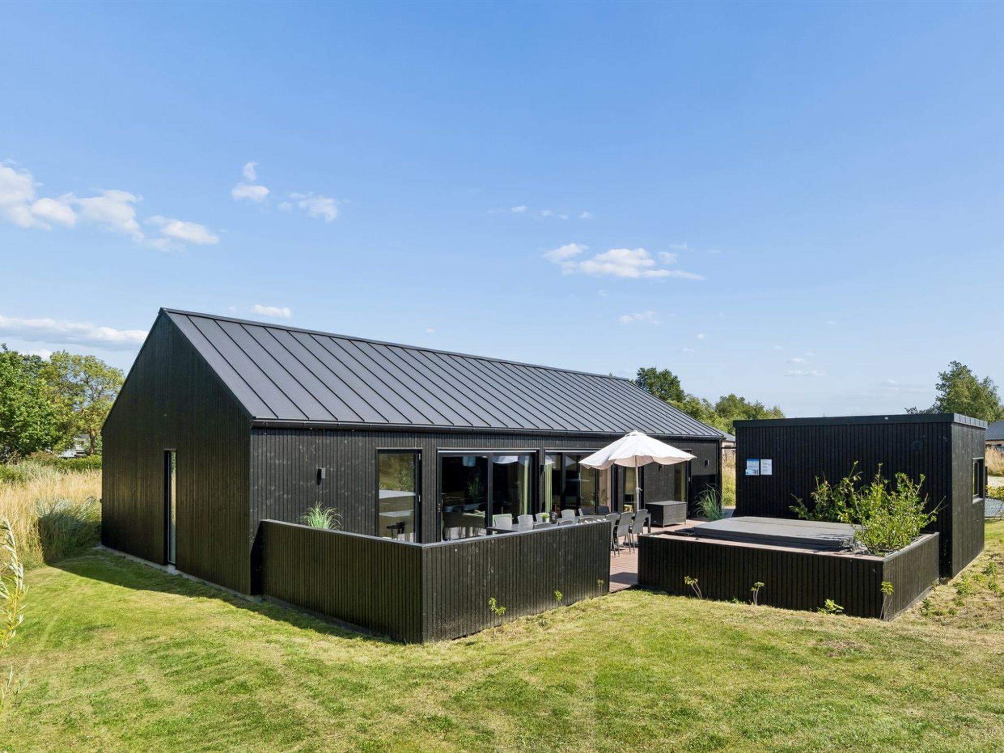 Un edificio moderno con techo inclinado, ventanas grandes y un patio con mobiliario exterior.