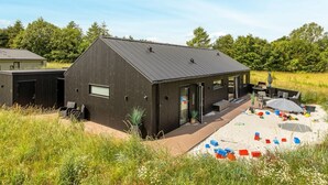 A modern building with a sloped roof, large windows, and a covered outdoor area with seating and toys. - "Artur" - 800m from the sea by Interhome (Glesborg)