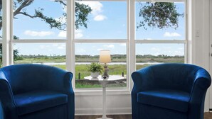 A room with two blue armchairs, a small white table with a lamp, and a view of a natural landscape through large windows. - Waterfront Serenity, Steps to Beach, Fire Pit, BBQ (St. Augustine)
