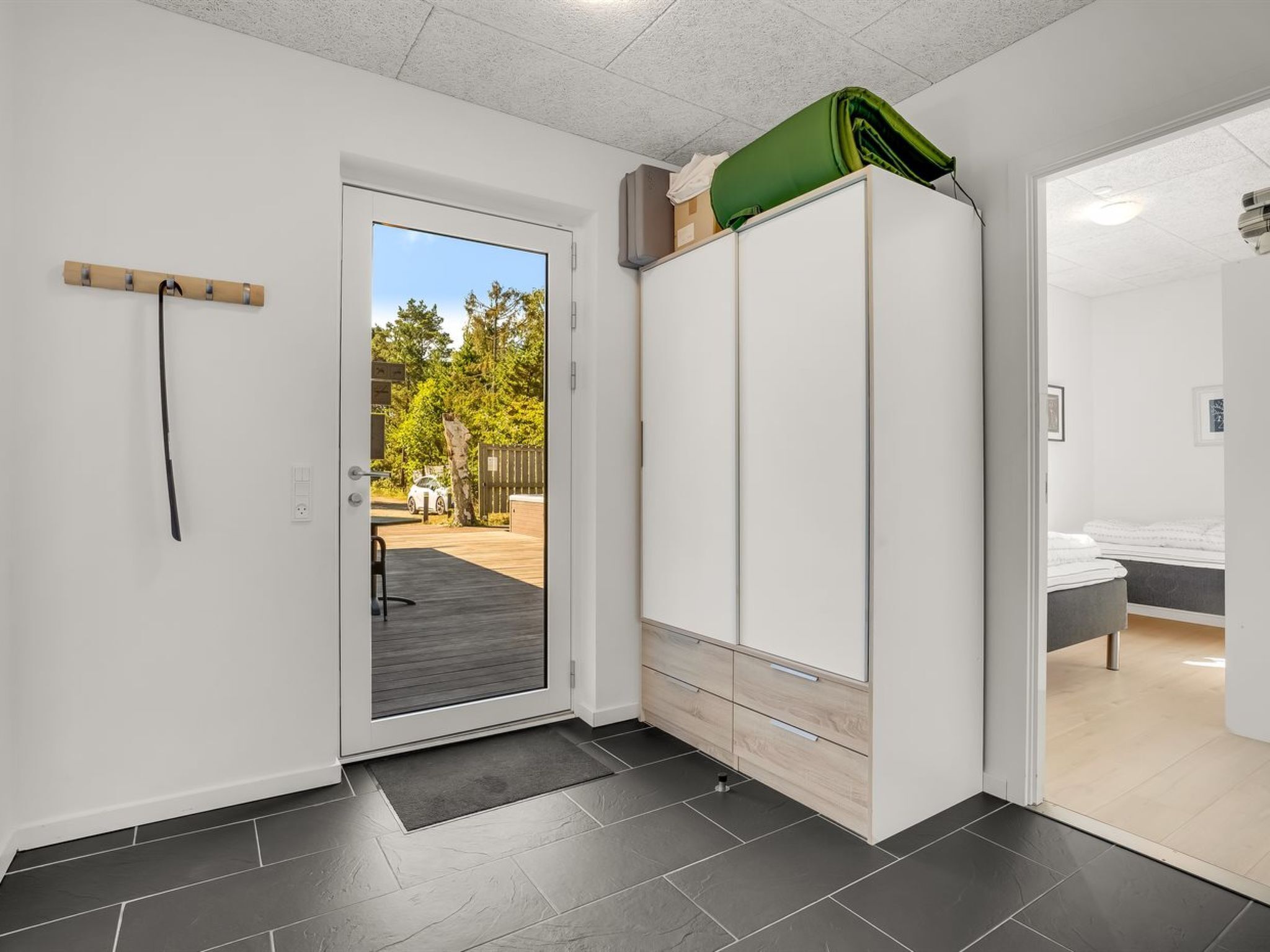 Quarto compacto com porta deslizante para área externa, guarda-roupa com várias gavetas e uma cama no quarto vizinho.