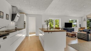 Eine moderne Küche mit weißen Schränken, einer Kochinsel mit Holztischplatte und einem Essbereich mit Sofa und Fernseher.