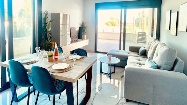 Un salon moderne avec un coin repas, de grandes fenêtres et un canapé gris.