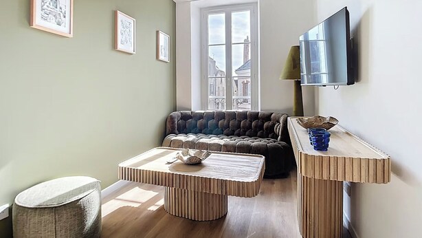 A modern living room with a sofa, a coffee table, and a TV mounted on the wall. - Amazon Suite (Montargis)
