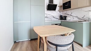 A compact kitchen with a wooden table and a chair, a built-in microwave, and a coffee maker. - Amazon Suite (Montargis)