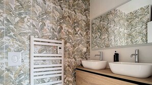 A bathroom with a wooden vanity, two sinks, a mirror, and a wall-mounted towel rack. - Amazon Suite (Montargis)