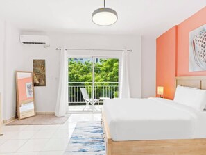 A hotel room with a bed, a balcony with a view, a painting on the wall, and an air conditioning unit.