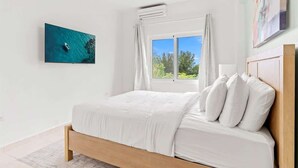 Een slaapkamer met een bed, een raam met gordijnen, een airconditioner en een schilderij aan de muur.