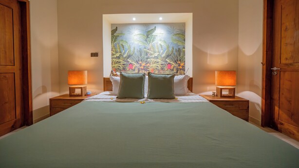 Une chambre avec un grand lit, deux tables de chevet avec des lampes et une fresque murale.