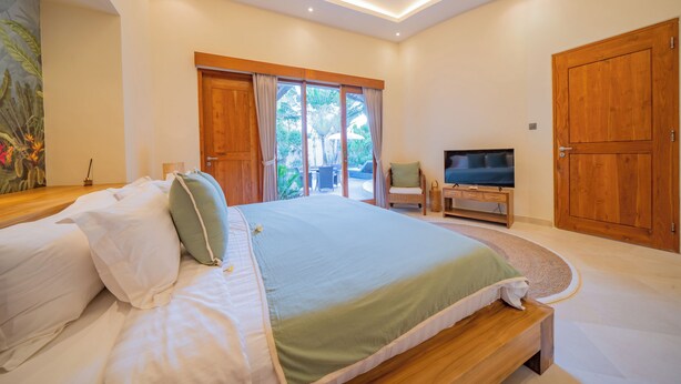 A bedroom with a large bed, a TV, and a sliding glass door leading to an outdoor area. - Luxury Balinese style villa with AC in Seminyak- 5BR for ultimate relaxation (Bali)