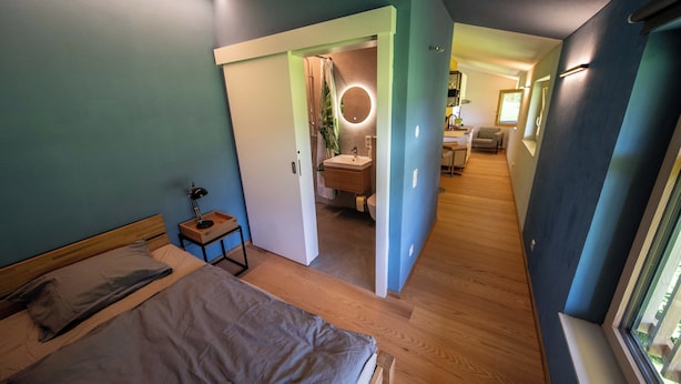 A bedroom with a bed, bedside table, and a view of the bathroom. - Studio Terra Salzburg Ecosuite (Altenmarkt im Pongau)