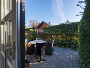 An outdoor patio with a round table and chairs, surrounded by a hedge and a brick floor. - Apartment Borné by Interhome (Zoutelande)