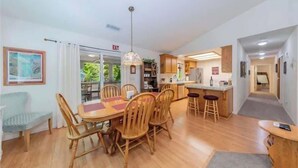 A spacious dining area with wooden furniture, a kitchen with a bar, and a view of greenery outside. - The Lady Bug Family Retreat (Mariposa)