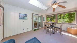 A spacious room with a ceiling fan, a skylight, a dining area with a table and chairs, and a view of greenery outside. - The Lady Bug Family Retreat (Mariposa)