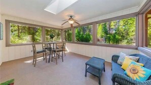 A sunroom with a ceiling fan, large windows, a dining table with chairs, and a sofa with a sunflower cushion. - The Lady Bug Family Retreat (Mariposa)