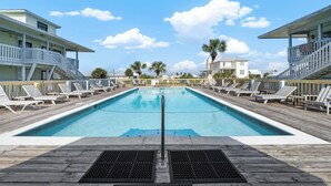 A rectangular pool with a wooden deck, surrounded by lounge chairs and a wooden fence.