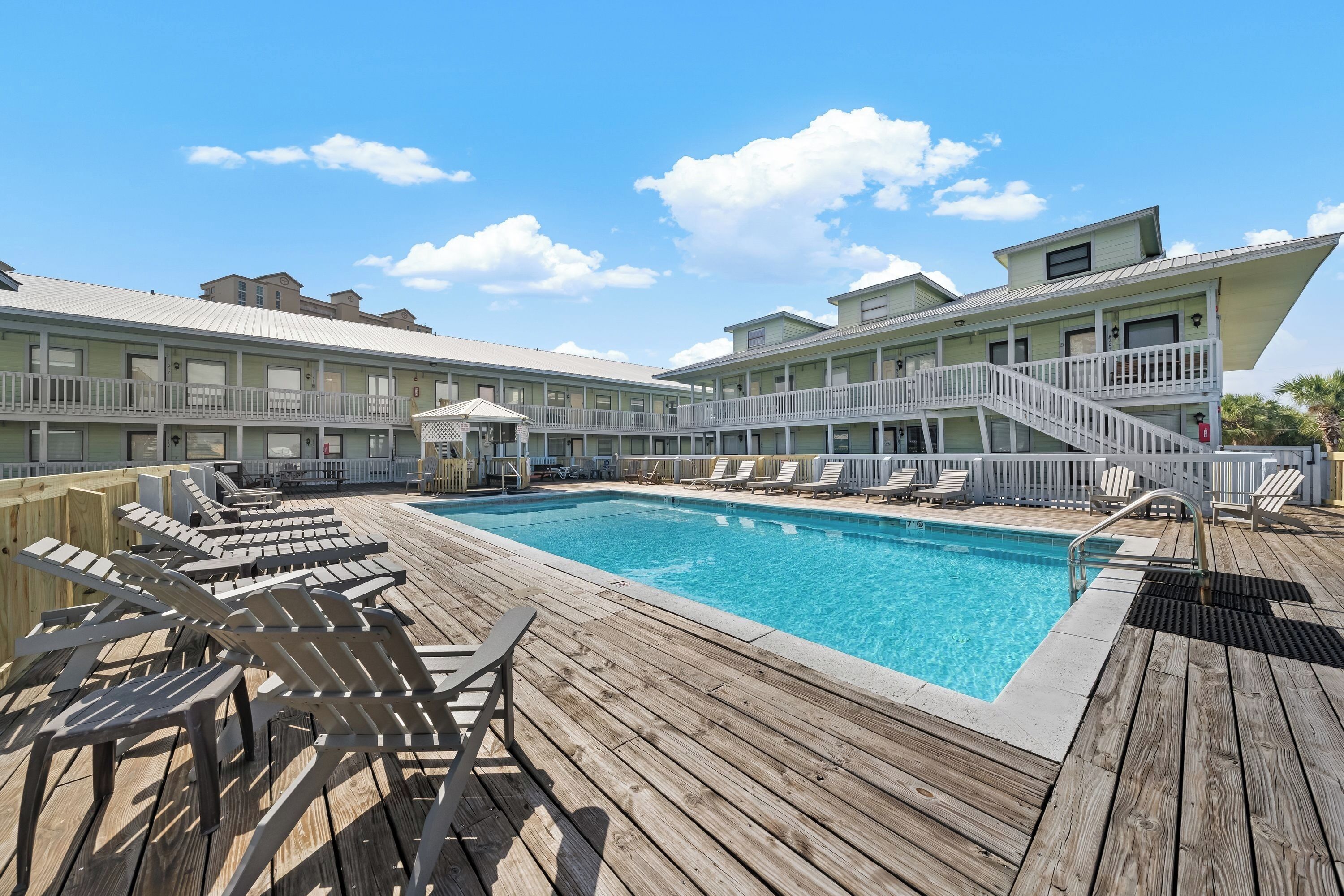 A poolside area with wooden deck chairs, a swimming pool, and a building with balconies.