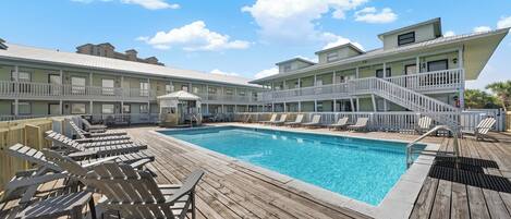 A poolside area with wooden deck chairs, a swimming pool, and a building with balconies.