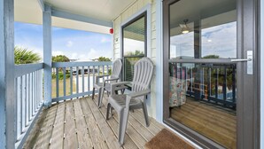 A covered porch with a view of the beach, two Adirondack chairs, and a sliding glass door.