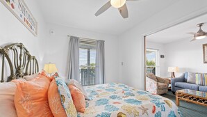 A bedroom with a bed, a chair, a sofa, a ceiling fan, and a window with curtains.