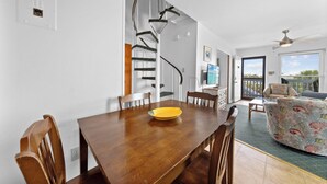 A dining area with a wooden table, chairs, a yellow bowl, a spiral staircase, and a view of the outdoors.
