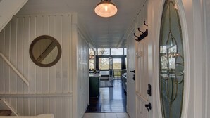 Un couloir avec un escalier en bois, un miroir rond, une porte en verre dotée d’un cadre décoratif et une vue sur un coin repas.