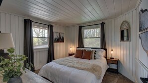 Une chambre à coucher avec un grand lit, deux tables de chevet avec des lampes, une fenêtre avec des rideaux et un miroir fixé au mur.