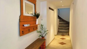 A hallway with a wooden bench, a wall-mounted shelf with a bowl, a potted plant, and a staircase.