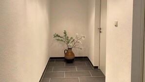 A hallway with a tiled floor, a vase with flowers, and a door.