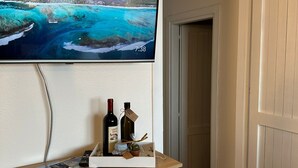 A flat-screen TV mounted on a wall displaying a scenic ocean view, a wooden counter with a remote control, and two bottles of wine.