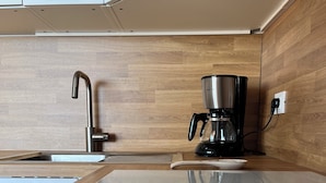 A modern kitchen with a stainless steel sink, a black coffee maker, and wooden cabinetry.