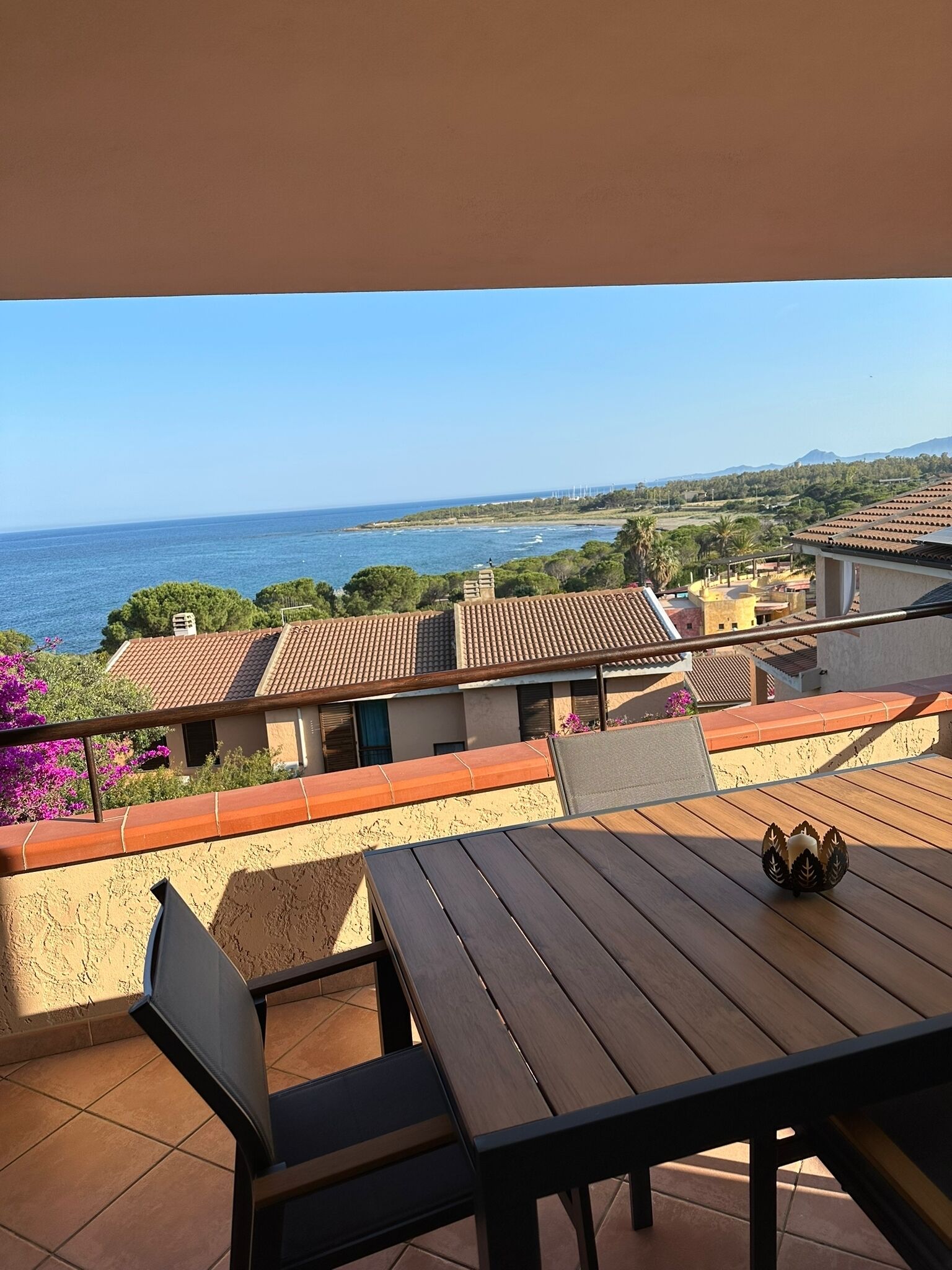 A terrace with a view of the sea, featuring a wooden table and chairs, and a small decorative item on the table.