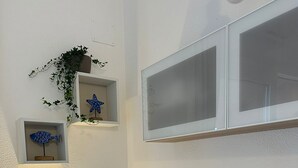 Ein Zimmer mit einem beigen Sofa, zwei blauen Kissen, einem kleinen weißen Tisch mit einer Lampe und Wandregalen mit Dekoration.