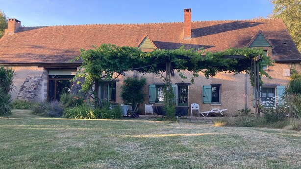 A stone house with a brick roof, a covered outdoor seating area, and a garden.