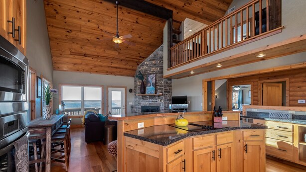 A spacious kitchen with wooden cabinets, a large island, and a stone fireplace. - Winston's View: Mountain Views, Fire Pit, Hot Tub (Jasper)
