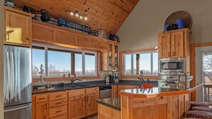 A modern kitchen with wooden cabinets, stainless steel appliances, and large windows. - Winston's View: Mountain Views, Fire Pit, Hot Tub (Jasper)