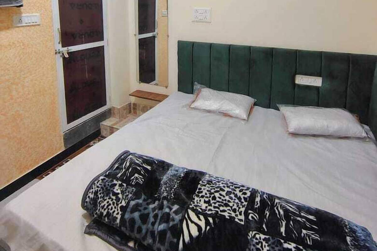 A bedroom with a bed, a green headboard, a window with a view, and a wall-mounted air conditioner.