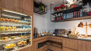 A modern kitchen with a buffet area, wooden cabinets, and a variety of food items. - Maitria Hotel Rama 9 Bangkok  (Bangkok)