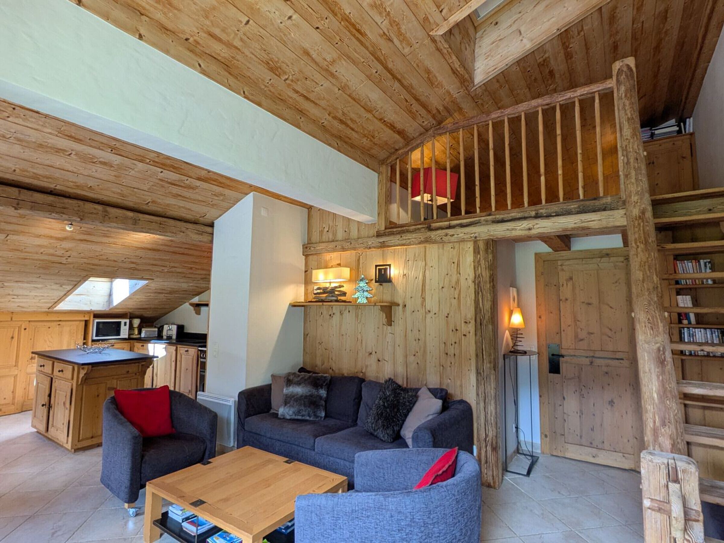 A cozy living area with a wooden ceiling, a sofa set, a coffee table, and a kitchen area with a microwave.