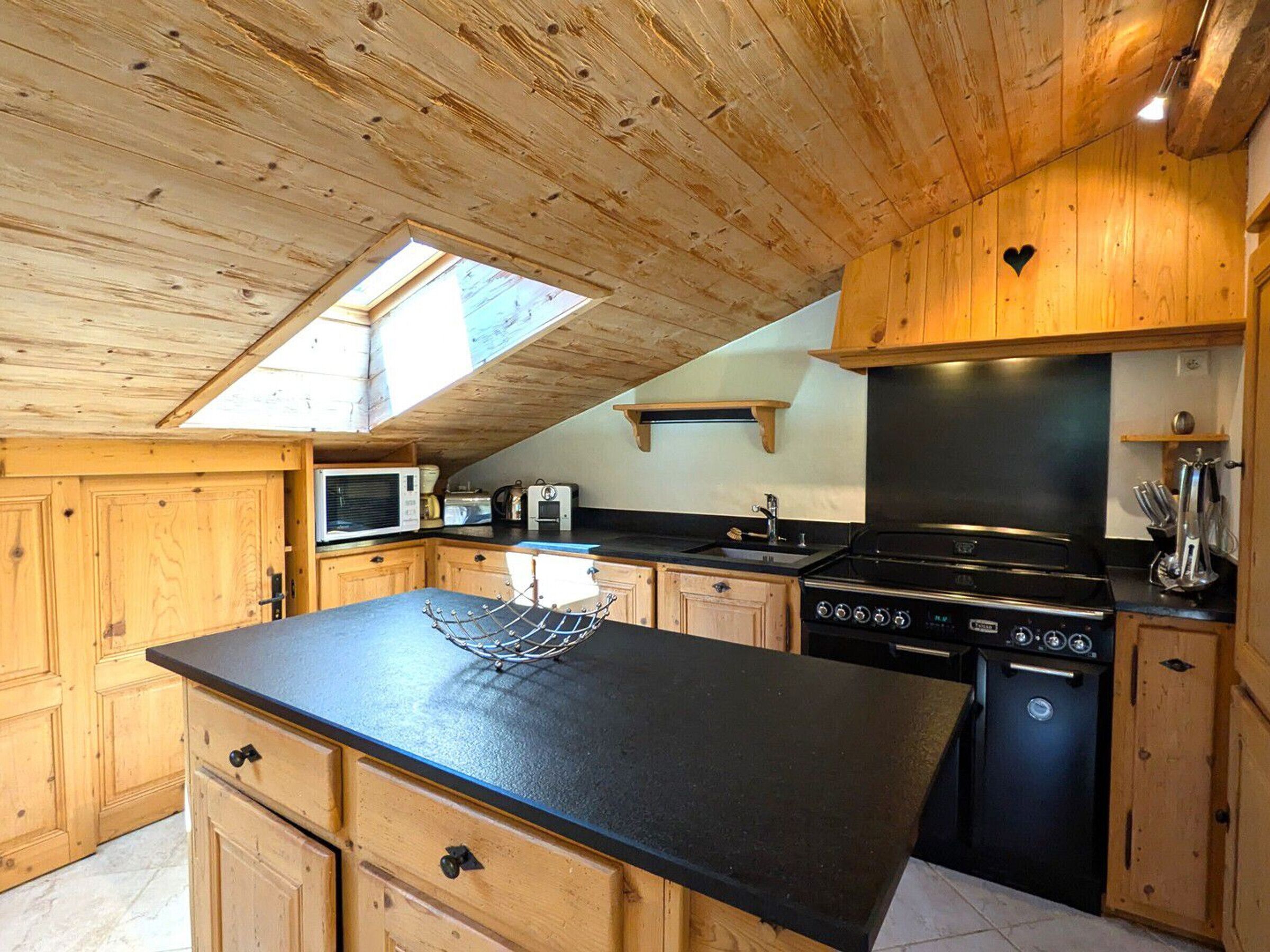 A compact kitchen with wooden cabinets, a black countertop, a built-in oven, and a skylight.