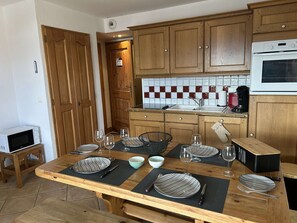 Uma cozinha com armários de madeira, painel de azulejos e uma mesa de jantar posta para quatro, com pratos, copos e talheres.