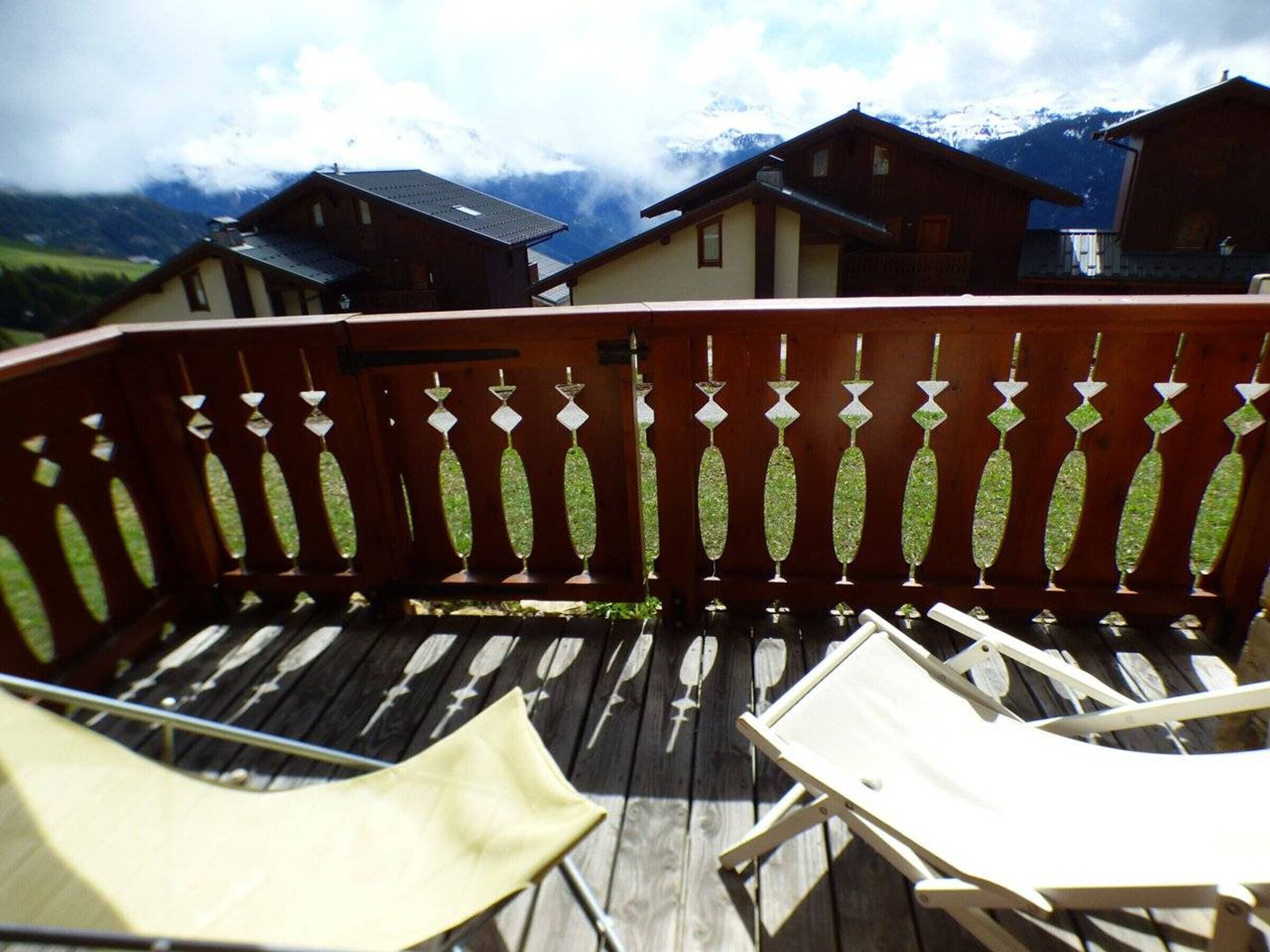 A wooden deck with two lounge chairs and a railing with decorative elements.