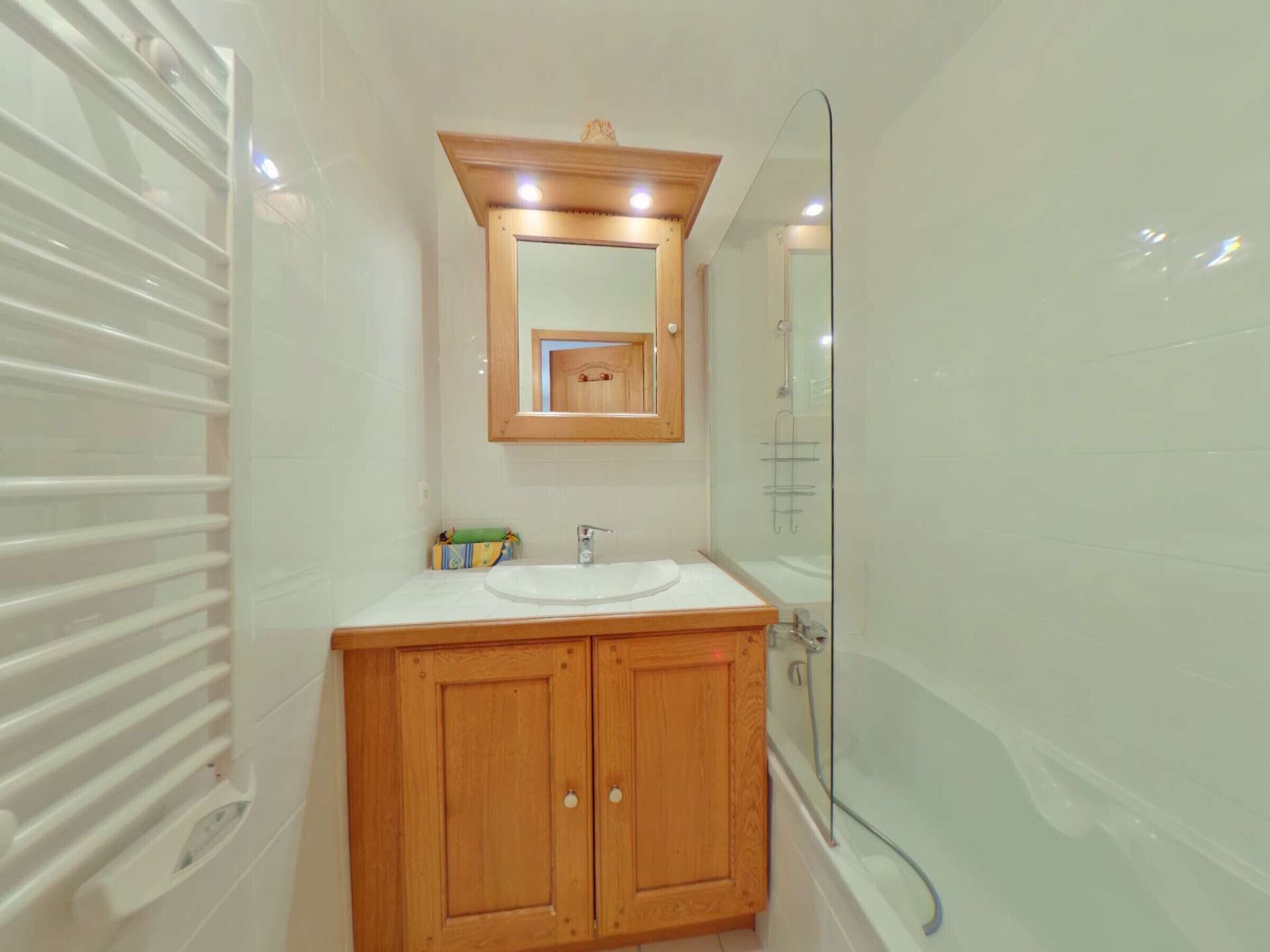 Ein Badezimmer mit einem Holzbadschränken, einem weißen Waschbecken, einem Spiegel und einer Glasdusche.
