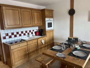 A kitchen with wooden cabinets, a tiled backsplash, and a dining area with a wooden table set for two.